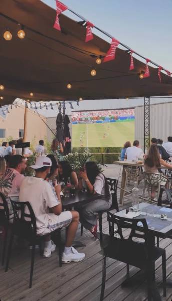 Plan de la terrasse du restaurant avec diffusion du match de foot de la coupe du monde 2026 sur l'écran géant.