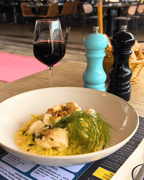 Table dressée avec verre de vin rouge, plat de poisson blanc et sel poivre décoratifs.